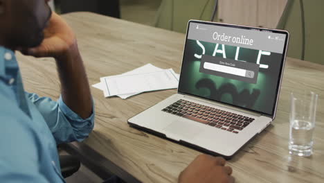 African-american-man-at-table-using-laptop,-online-shopping-during-sale,-slow-motion