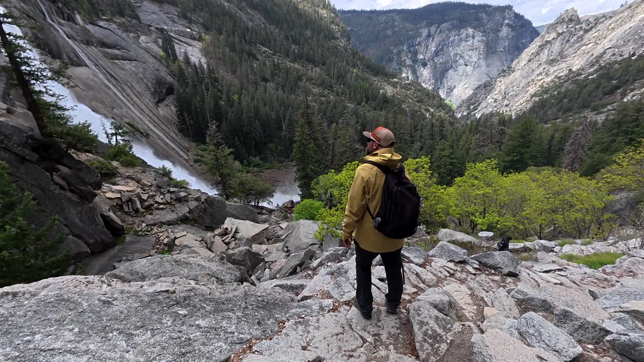 Escursionista che scende un sentiero di montagna roccioso verso una cascata