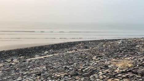 Cinematic-shot-of-a-shore-line-covered-with-stones-near-an-ocean-in-Tajpur,-Bengal,-India