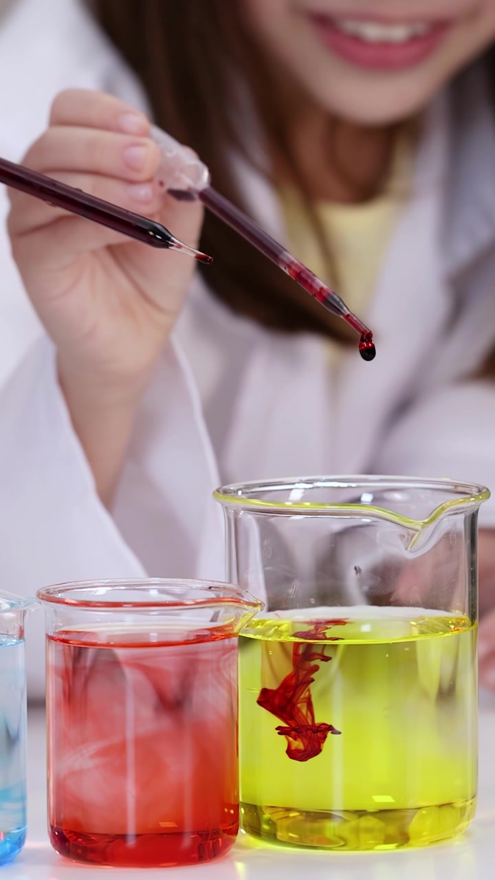 Close-up of students using pipettes to drop liquid into beakers during a classroom science lesson.