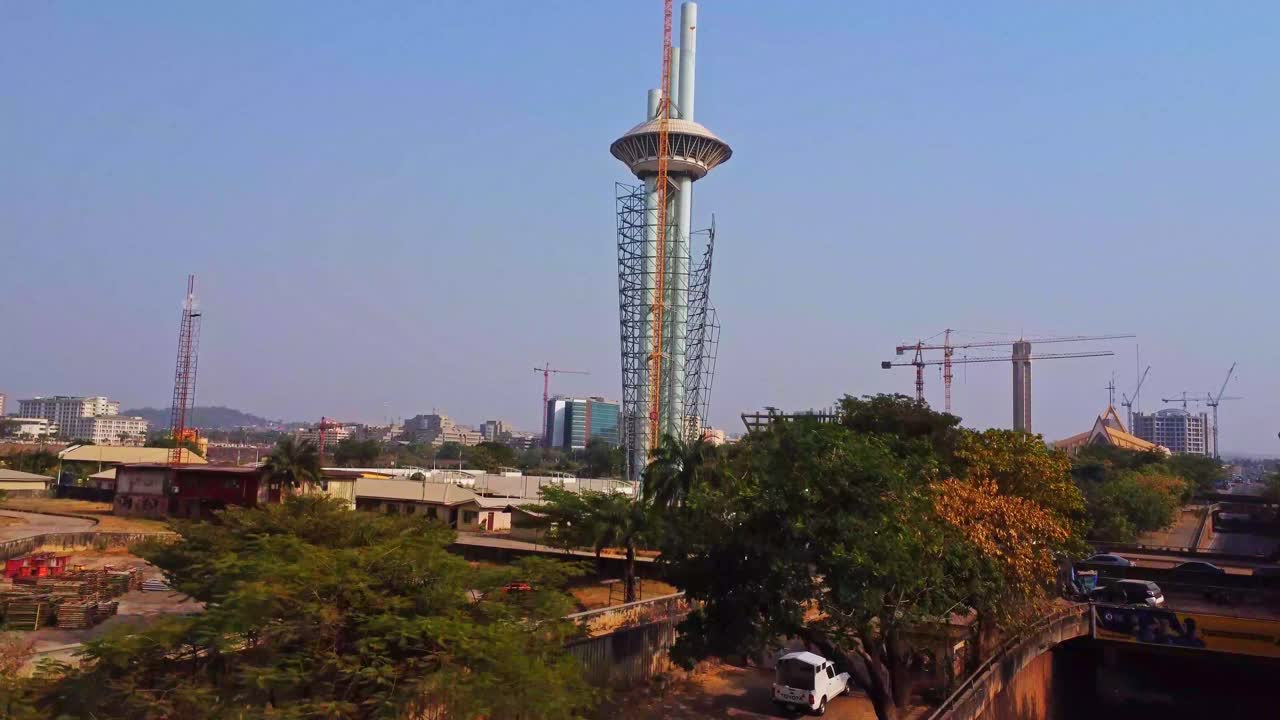 Drone flying towards the tall Millennium Tower in Abuja, the capital city of Nigeria, Africa. Large cranes stand on the construction site of the cultural centre