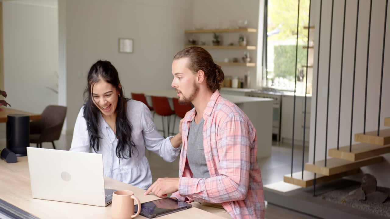 Young happy couple are looking at laptop together, in kitchen at home
