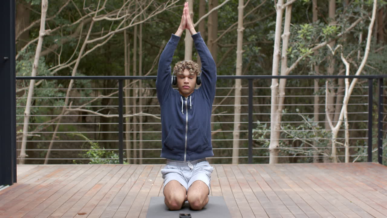 Young man meditating on yoga mat outdoors, wearing headphones, enjoying nature