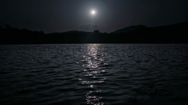 Riflesso di una luccicante luna piena che danza sulla superficie di un lago di notte, la brezza crea increspature