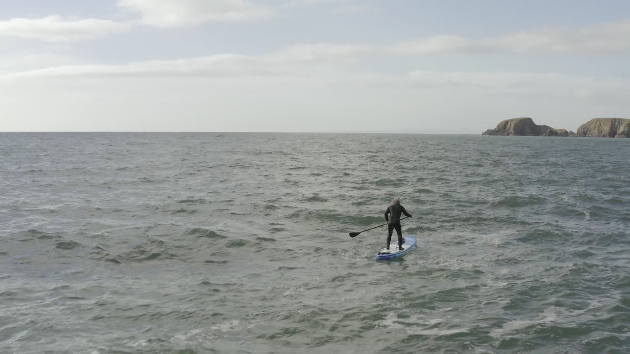 sobrevuelo aéreo de sup paddleboard masculino en el océano gris entrecortado cerca del acantilado