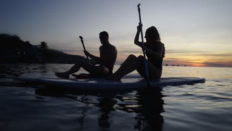 silhouetted couple paddleboarding at sunset