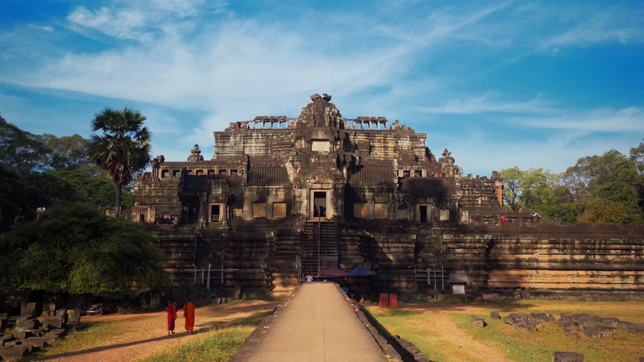 Monks in red robes standing near the main entrance of Baphuon Hindu temple, Cambodia, slow motion
