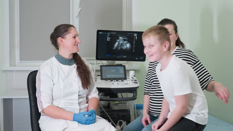 medical doctor and mother seated as young boy walks into room to join her on clinical bed, depicting a family setting in a medical consultation room with positive atmosphere in a clinical environment
