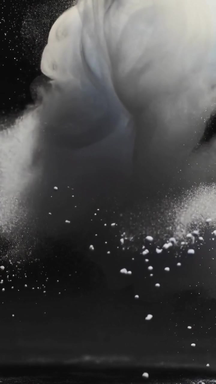 Video verticale: Pennacchio bianco che cade formando una colonna piegata in un serbatoio al rilascio, disperdendo fini particelle.