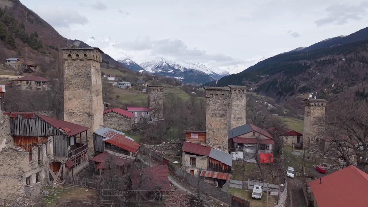 Filmagem aérea capturando a beleza atemporal de Mestia, onde torres Svan históricas e casas tradicionais são cercadas pelas espetaculares Montanhas do Cáucaso cobertas de neve.