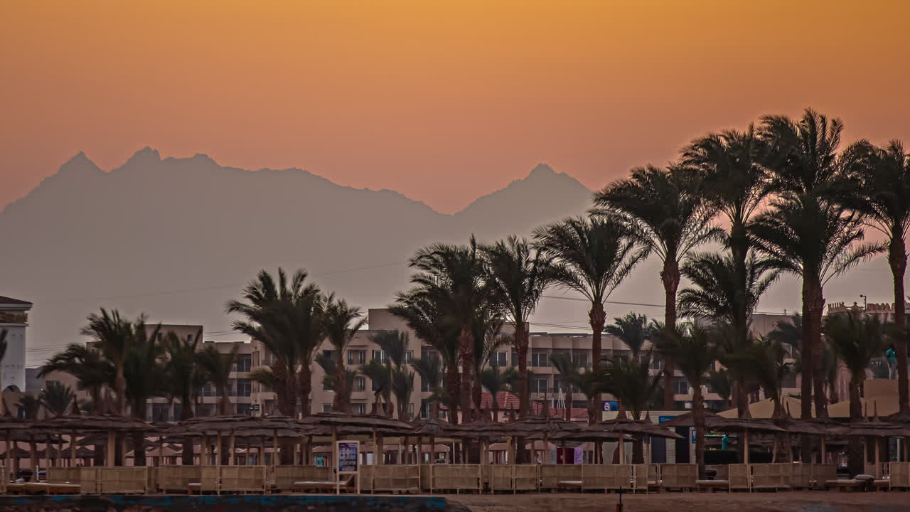Timelapse del tramonto di un resort sulla spiaggia a Hurghada, Egitto, con palme, edifici e sole arancione.