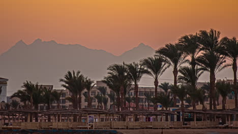 Sunset-Timelapse-of-Beach-Resort-in-Hurghada,-Egypt-with-Palm-Trees-and-Buildings-orange-sun