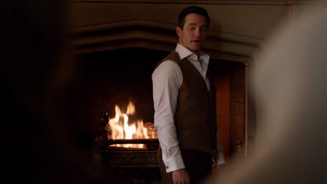 man in vest standing in front of a fireplace