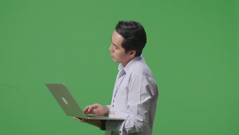 아시아 사업가의 측면 뷰는 만족하지 않고 녹색 화면 스튜디오에서 노트북 컴퓨터를 사용하는 동안 머리를 흔들고 있습니다.