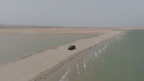 off-road suv driving on remote beach sandbar at masirah island, oman, aerial view