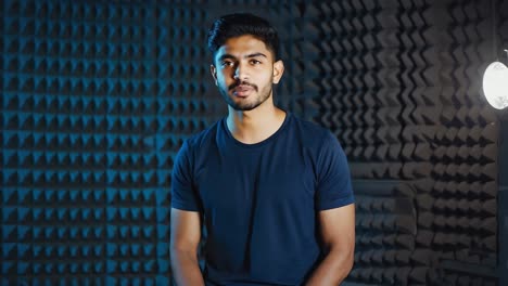 sound engineer smiling, taking break during recording session, standing in professional music studio with acoustic panels, softbox lighting surrounding workspace