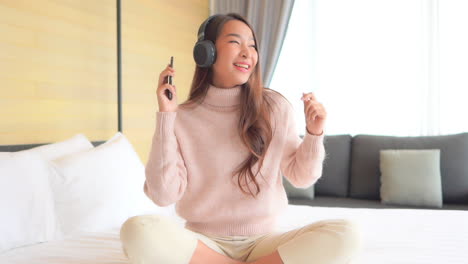 beautiful asian woman listening music with smartphone and headphones in bedroom