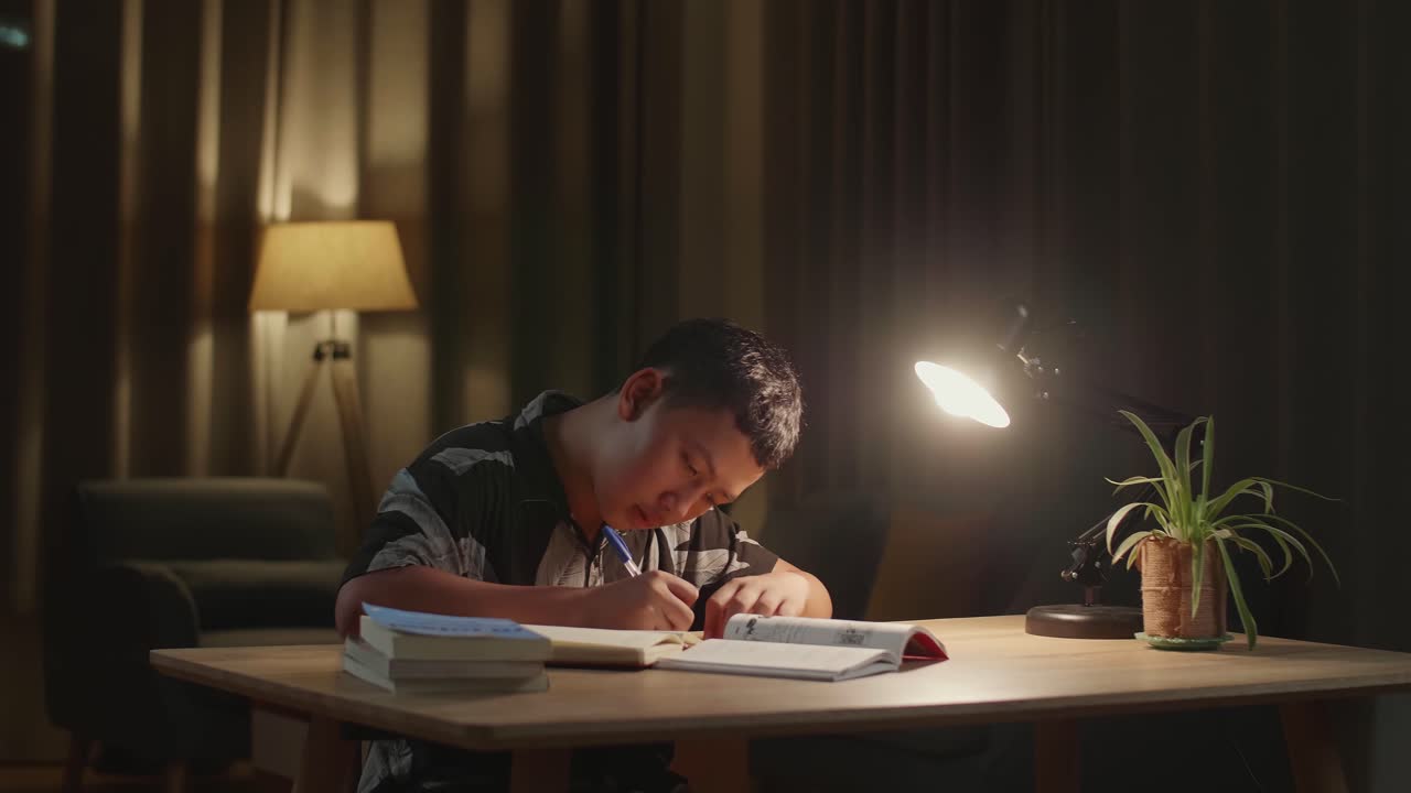 Asian Boy Is Studying At Home, Asia Child Writing While Sitting On The Table At Night
