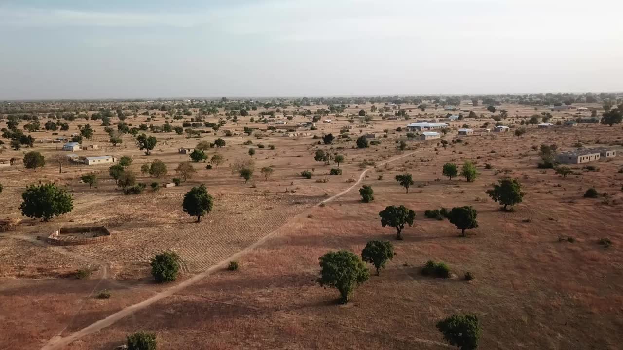 Vista aerea da drone di un paesaggio di savana arida nel nord del Ghana con sparsi insediamenti rurali, sentieri sterrati e alberi di karité durante la stagione secca