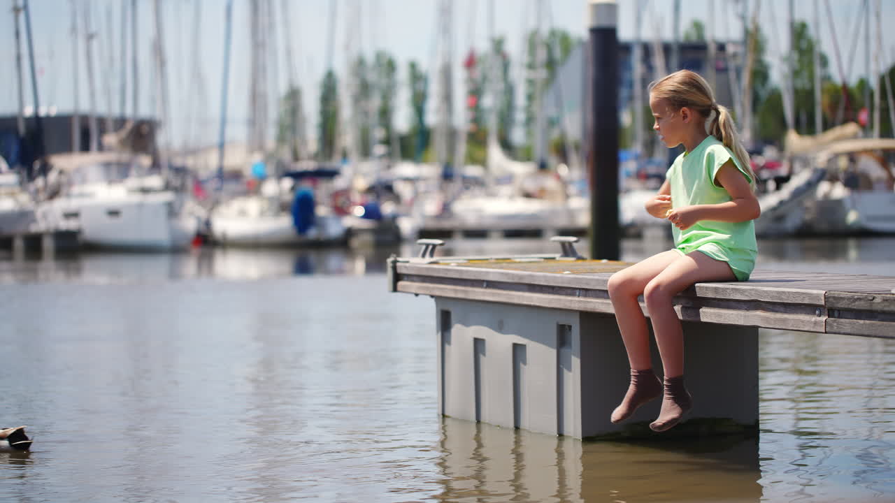 Junges Mädchen füttert eine Ente von einem Steg in einem Yachthafen