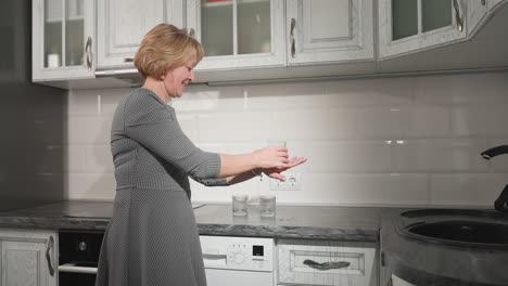 woman playfully placing glass cup with contents on the back of her palm while another glass cup rests on the countertop in kitchen, adding an elegant touch to home decor