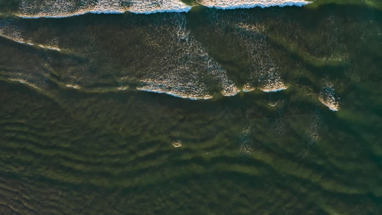 Aerial Top Down View of Foamy Ocean Waves Crashing Gently at Golden Hour