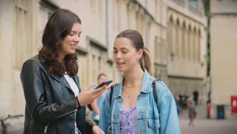 same sex female couple sightseeing follow map app on mobile phone as they walk around oxford uk