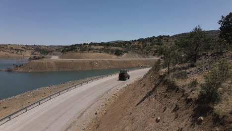 Drone-following-red-trucktor-slowly-driving-a-road-in-turkey-karaman-between-blue-lake-and-mountains-at-a-sunny-summer-though-curves