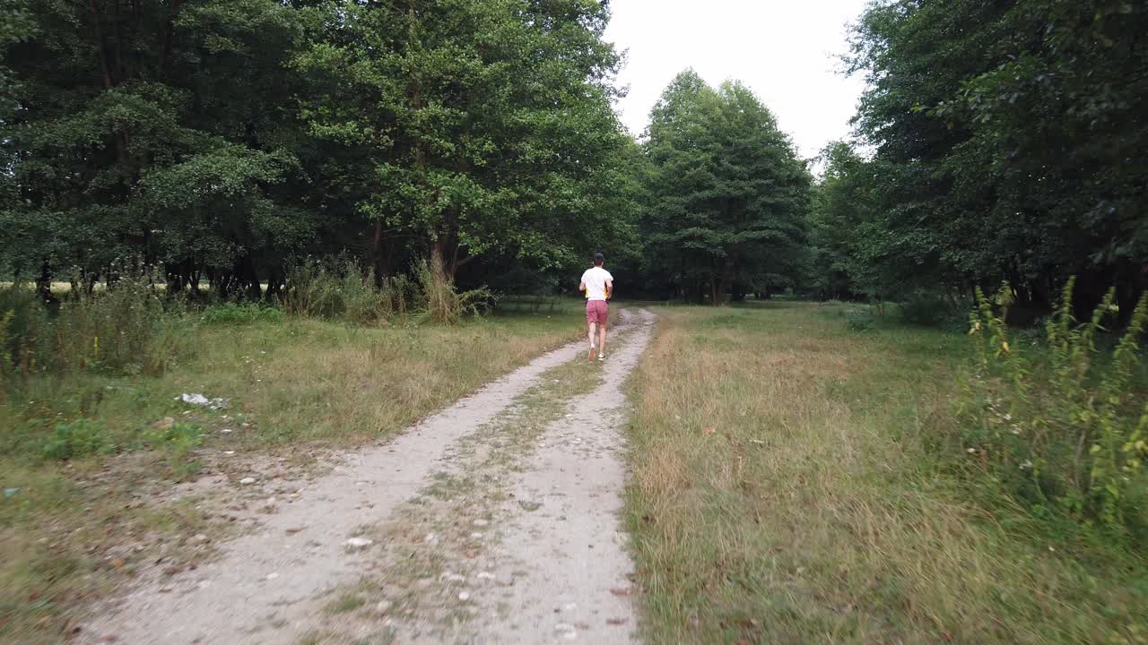 joven varón caucásico corriendo en el bosque por un sendero en verano