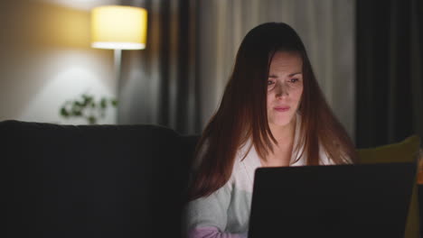 anxious woman sitting on sofa at home at night looking at laptop concerned about social media or bad news 9