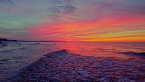 las olas del océano ruedan hacia la playa de arena con un cielo naranja brillante arriba