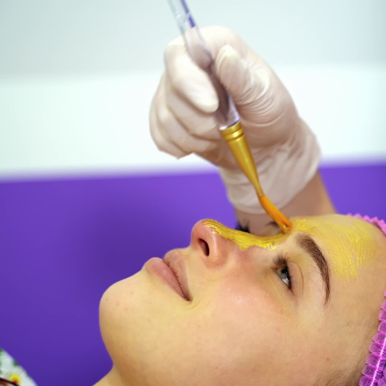 Beautician applies mask to the face of a young woman. Cosmetology. Close-up. Selective focus. Video from the top