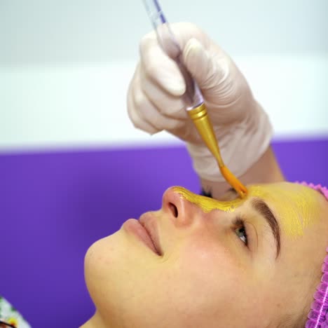 beautician applies mask to the face of a young woman. cosmetology. close-up. selective focus. video from the top