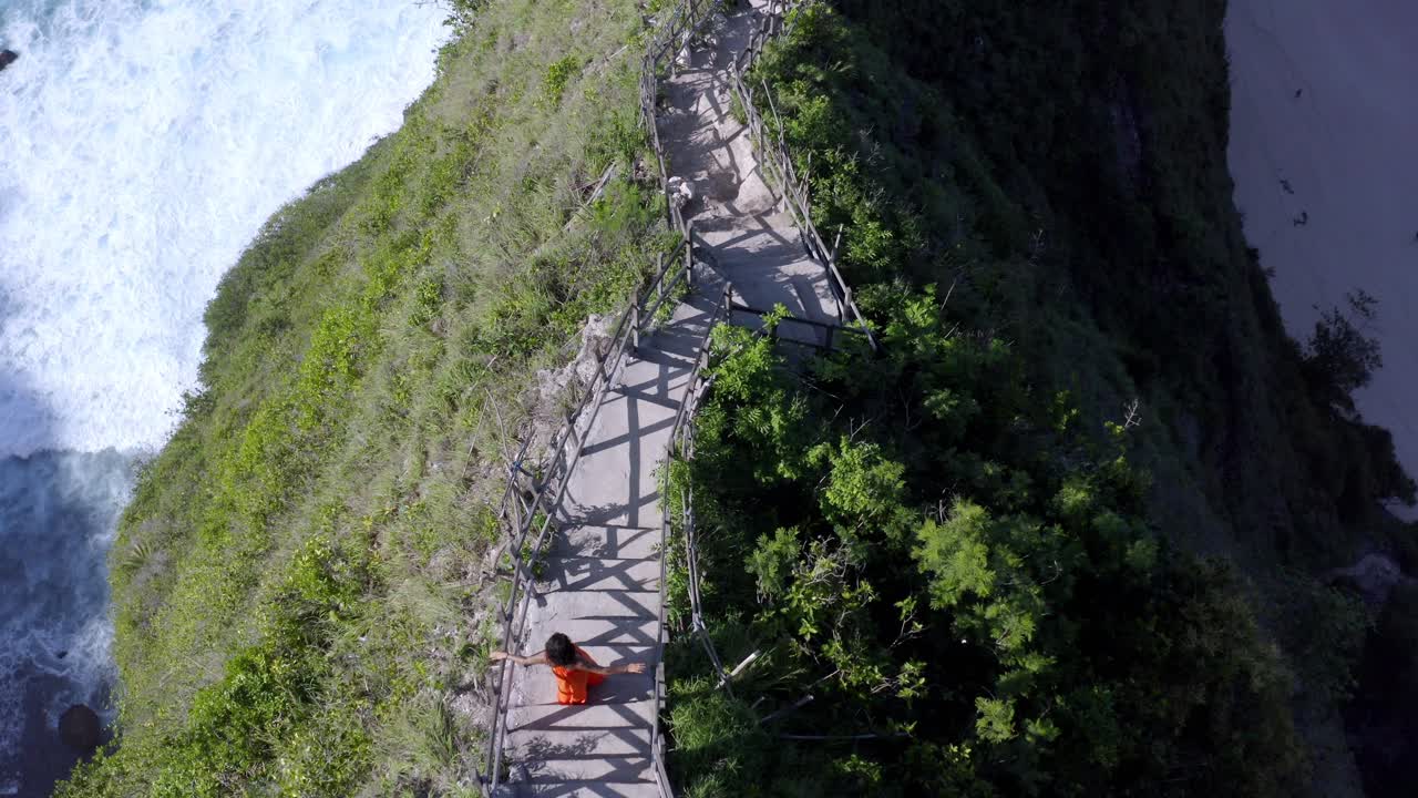 누사 페니다 섬 인도네시아 내림차순 계단, 공중 오버헤드 회전 뷰 샷의 켈링킹 해변에서 주황색 드레스를 입은 여성