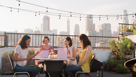 Female-Friends-Celebrating-Birthday-On-Rooftop-Terrace-With-City-Skyline-In-Background