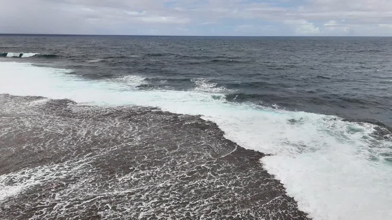 Static drone shot at Magpupungko Tidal Pool in Siargao, Philippines, showing ocean waves crashing over the reef along the Pacific shoreline under a partly cloudy sky