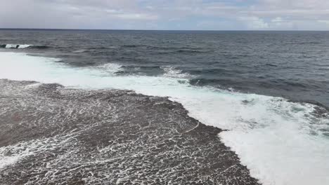 static drone shot at magpupungko tidal pool in siargao, philippines, showing ocean waves crashing over the reef along the pacific shoreline under a partly cloudy sky
