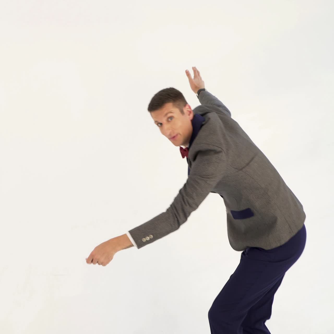humorist in gray suit with red bow tie is dancing in the similitude of dancer with ribbon in hand on white background in studio