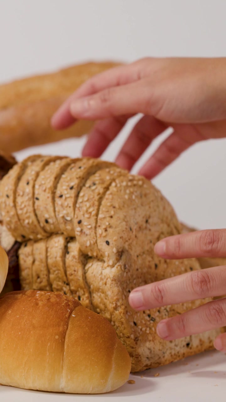 Primer plano de manos colocando pan multigrano en rebanadas entre baguettes y panecillos sobre fondo blanco