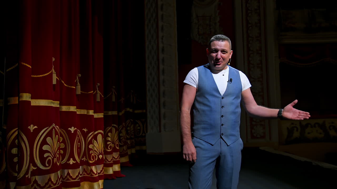 Showman entertains the audience under the light, front view. Big stage. Funny performer speaks to the camera. Active gestures on a stage.