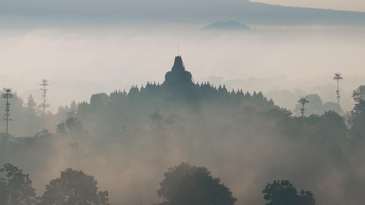 婆罗浮屠寺的雾中日出景象，周围环绕着森林和宁静的印度尼西亚风光。