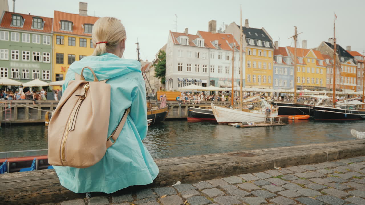 una mujer se sienta en el terraplén y admira los coloridos edificios a orillas del canal nyhavn i