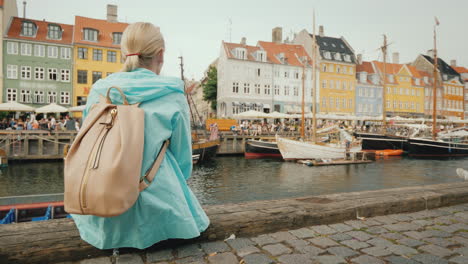 A-Woman-Sits-On-The-Embankment-And-Admires-The-Colorful-Buildings-On-The-Banks-Of-The-Nyhavn-Canal-I