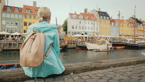 a woman sits on the embankment and admires the colorful buildings on the banks of the nyhavn canal i