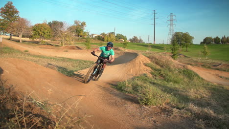 man on mountain bike whips around dirt trails in a bike park, before he whips in front of the camera