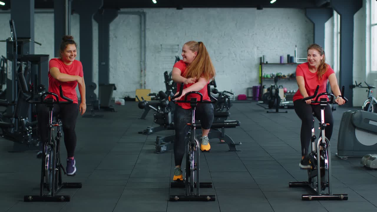 Group of smiling friends women class exercising training spinning on stationary bike at modern gym
