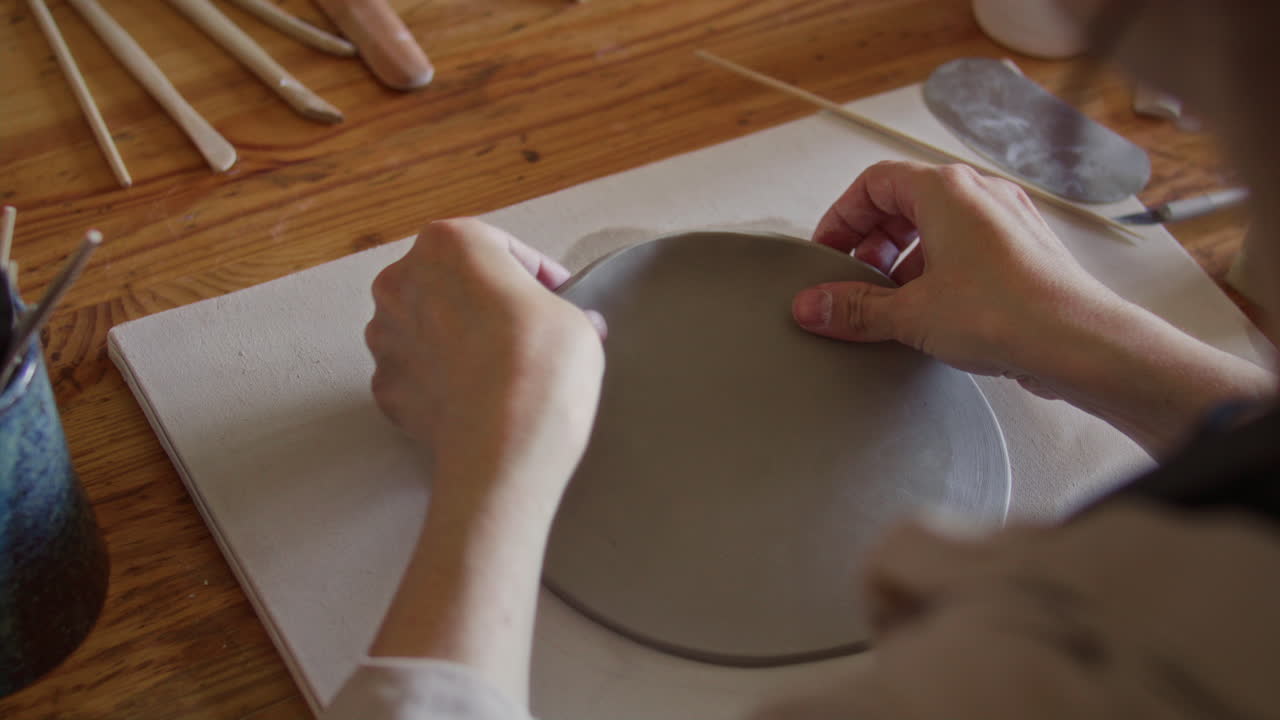Hands of Female Artisan Crafting Clay Plate on Wooden Table in Pottery