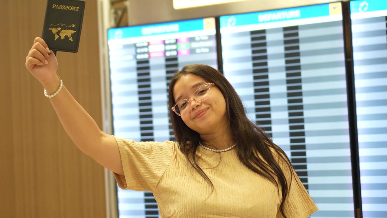 Inquadratura statica a campo medio di una giovane donna latina sui vent'anni in piedi davanti a un grande tabellone delle informazioni sui voli dell'aeroporto