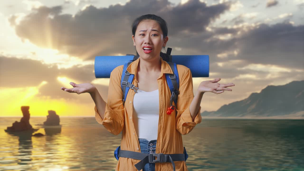 Nữ du khách đi bộ đường dài người châu Á tỏ vẻ khó hiểu, đeo ba lô leo núi, làm điệu bộ nghi ngờ và hỏi lý do trong khi đứng trên bãi biển lúc hoàng hôn