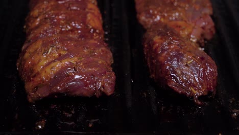 tilt up reveal of two raw beef steaks grilling on cast iron griddle, closeup